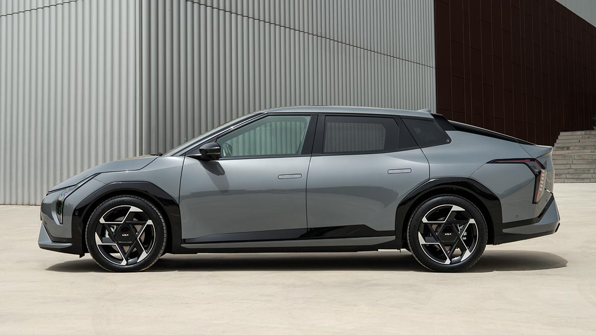 Side-on view of grey Kia EV4 electric hatchback parked in front of grey corrugated iron shed.