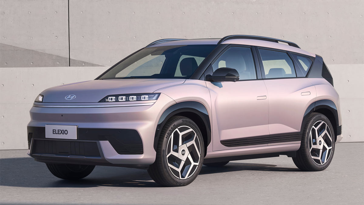 Pink Hyundai Elexio medium electric SUV parked in front of concrete wall.