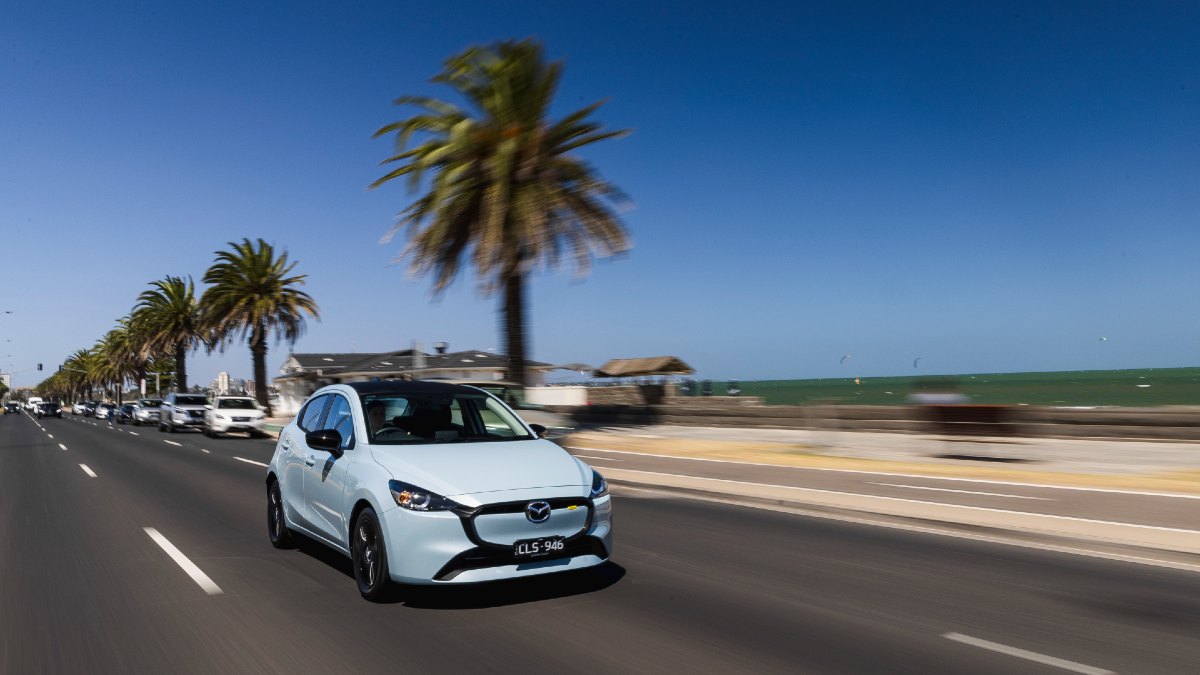 light blue Mazda2 driving by ocean