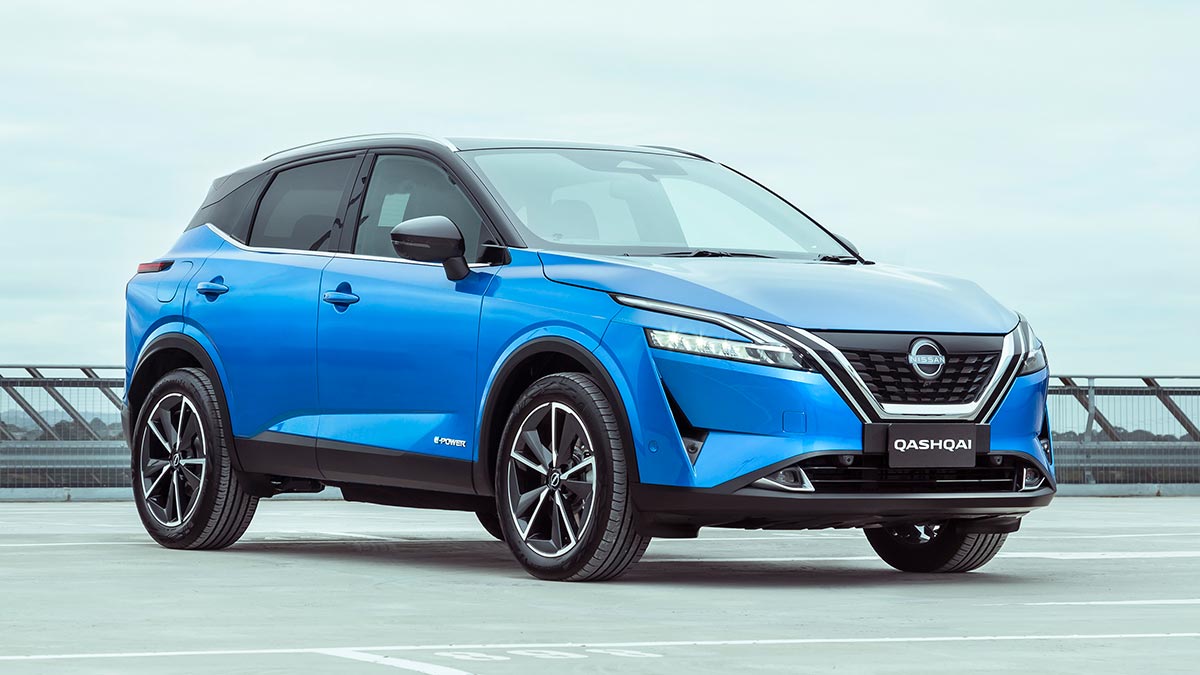 Blue Nissan Qashqai hybrid small SUV near barrier on rooftop carpark with cloudy skyline behind. 