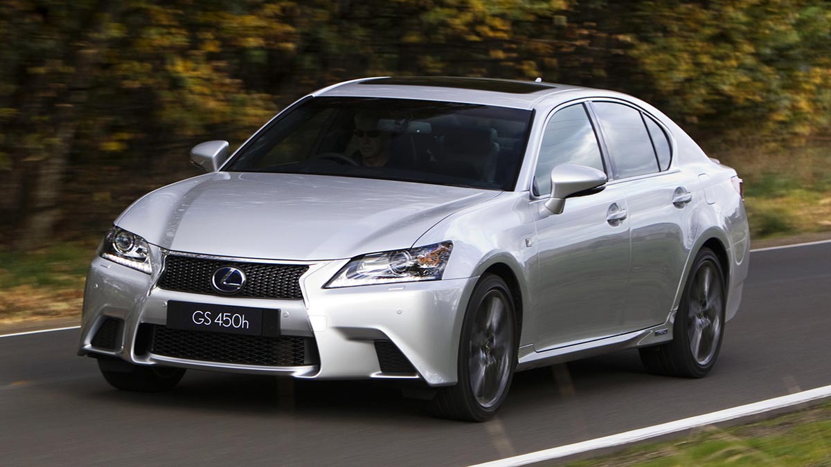 Silver Lexus GS450h luxury hybrid sedan driving on narrow single-lane tree-lined bitumen road.