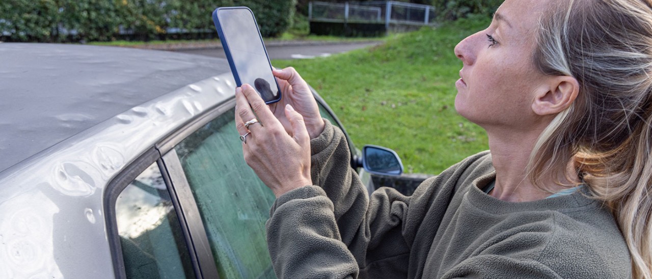 A woman takes a photograph of her hail-damaged car.