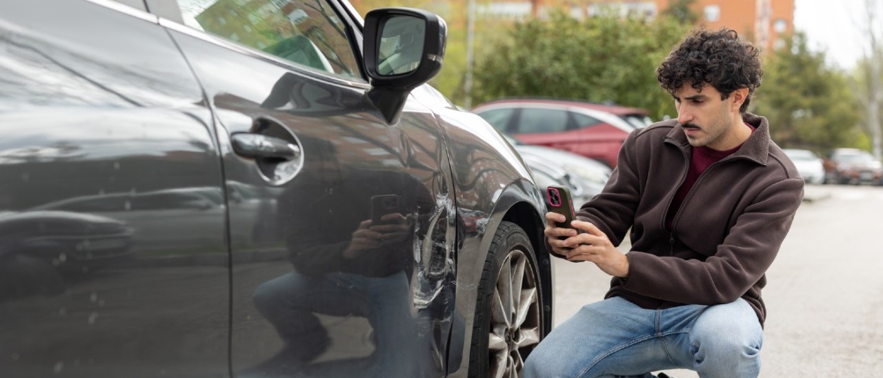 young man taking photo of damage to car after collision