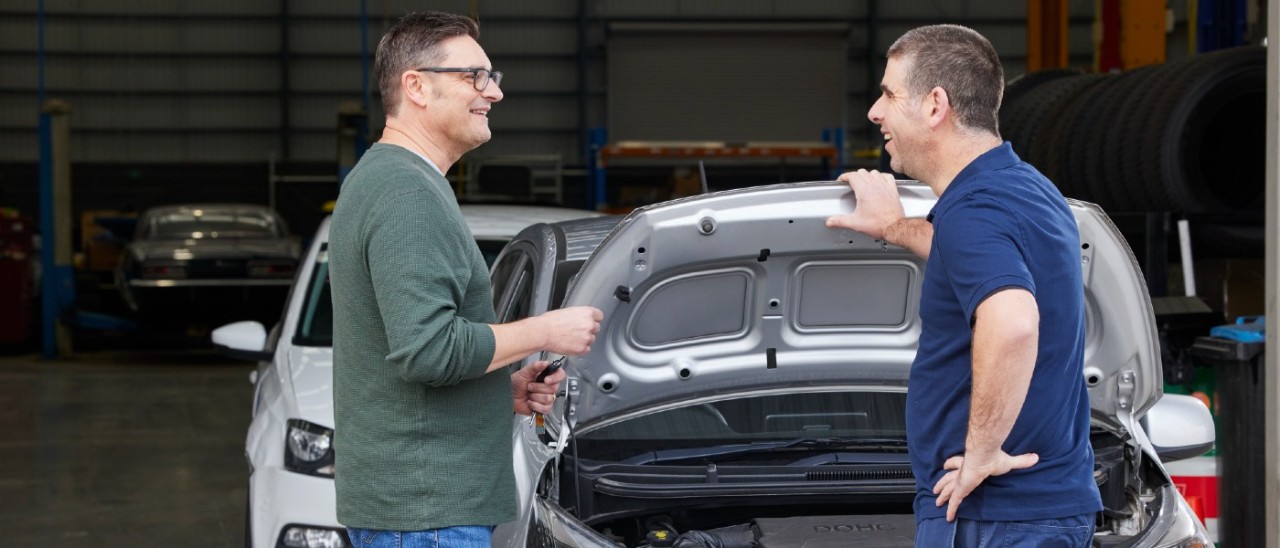 mechanic speaking to car owner in front of car with hood up