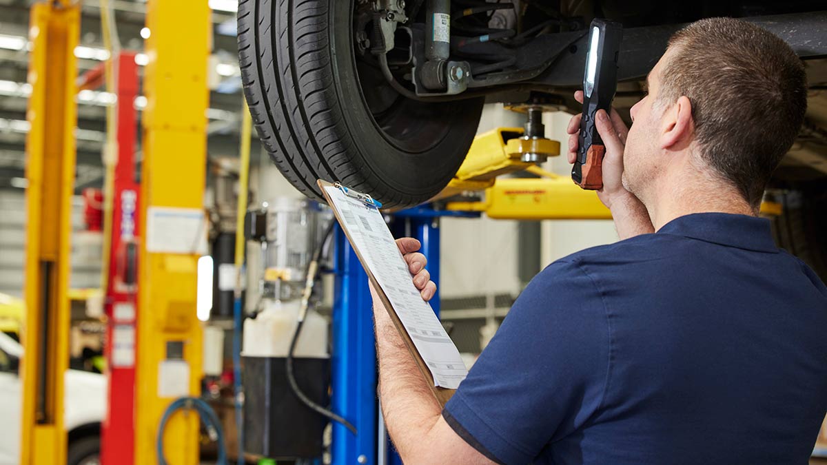 Technician at RACV accredited workshop conducting mechanical inspection with car on hoist.
