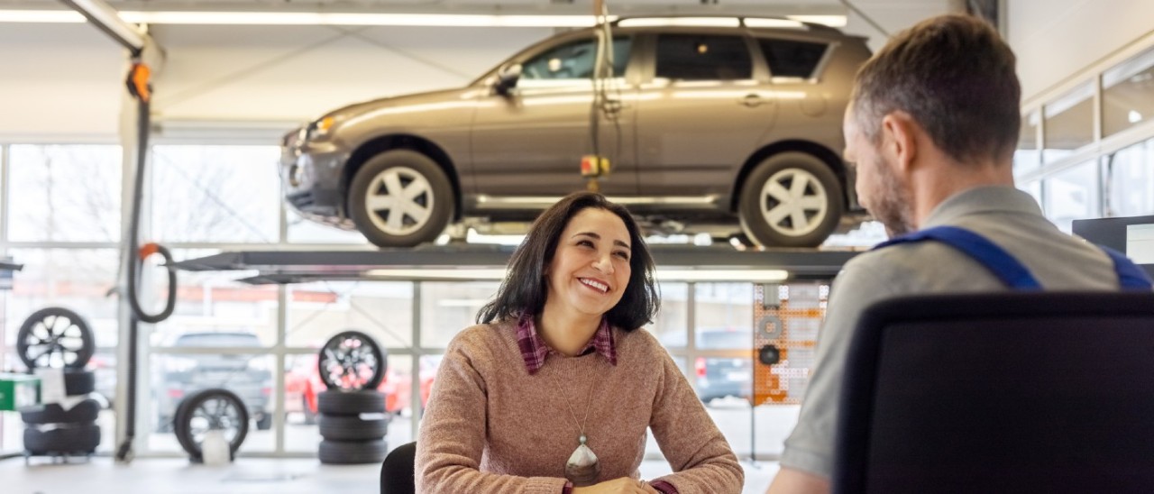 car mechanic speaking to car owner in workshop with elevated car in background