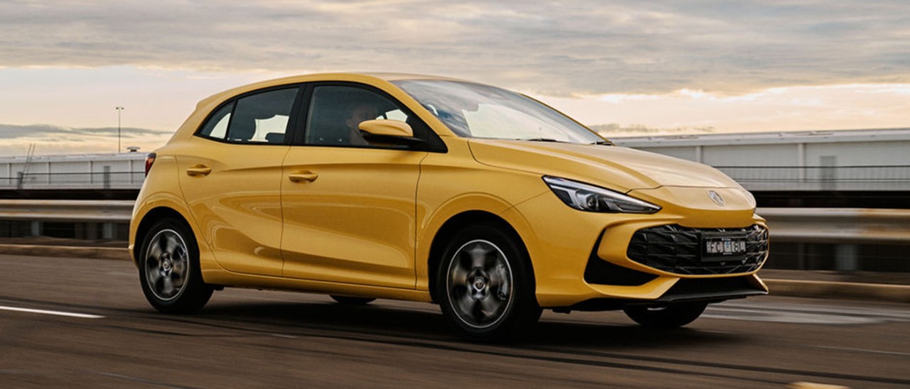 Yellow MG3 hybrid hatchback driving on multi-lane overpass with bright sky in background