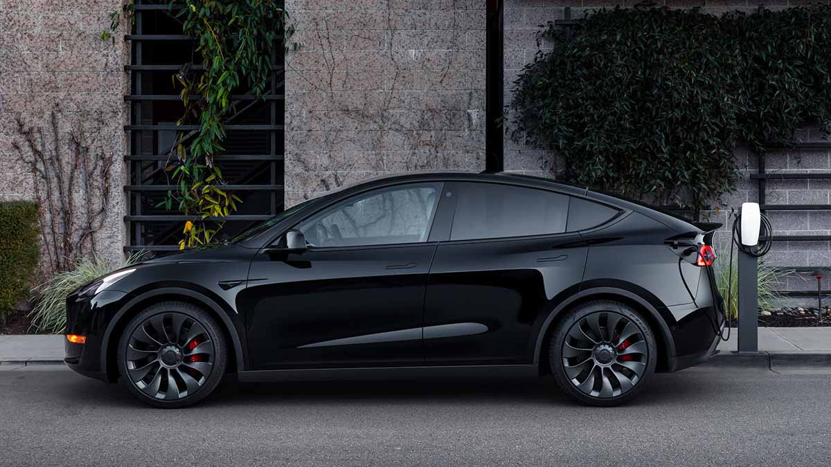 A black Tesla Model Y being recharged outside a home.