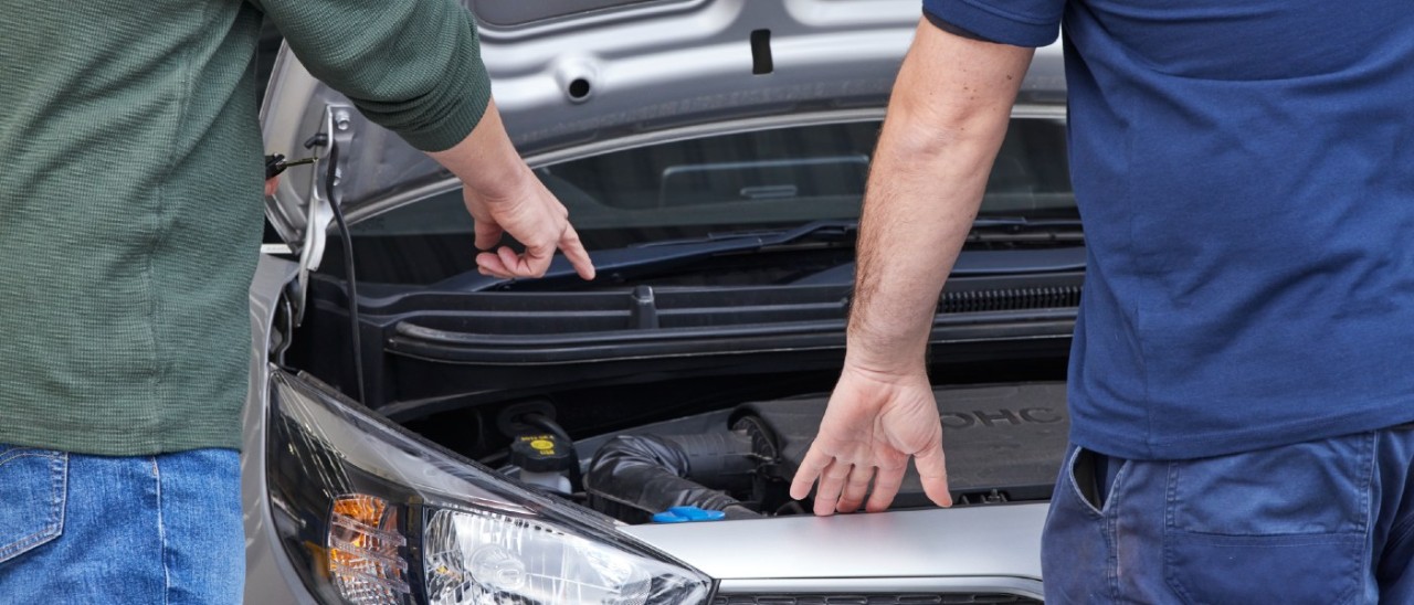 Two people pointing at and inspecting a car's engine under the bonnet