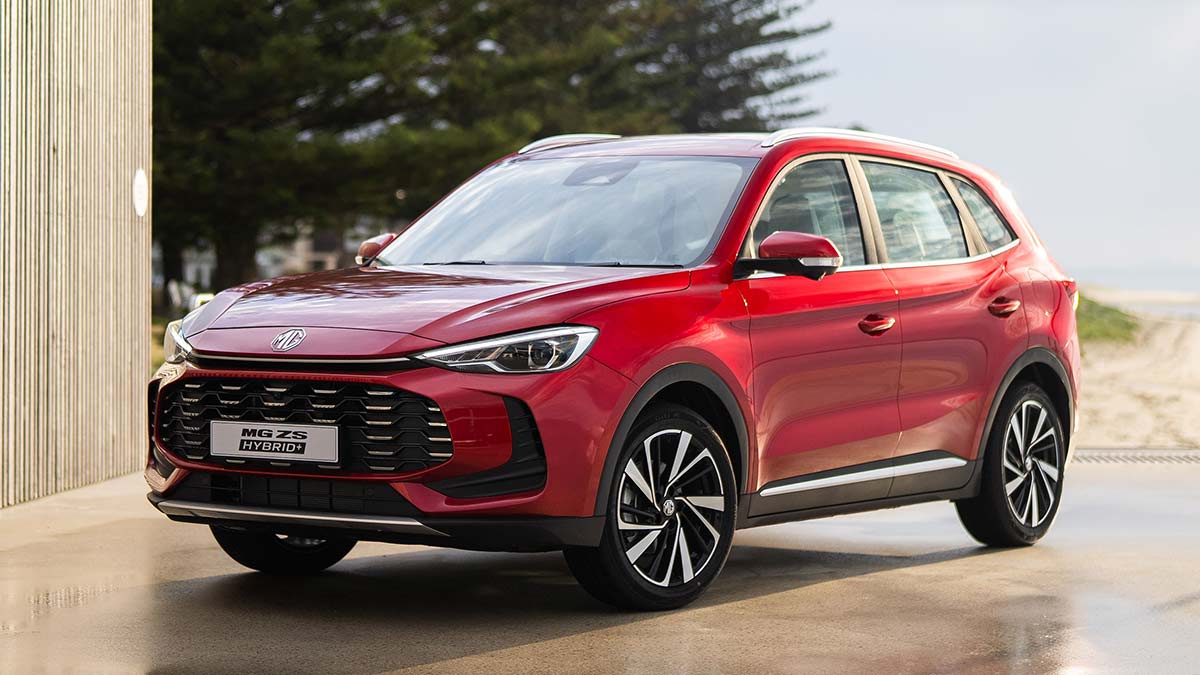 Red MG ZS Hybrid small SUV on concrete outside pavilion at beachfront location.