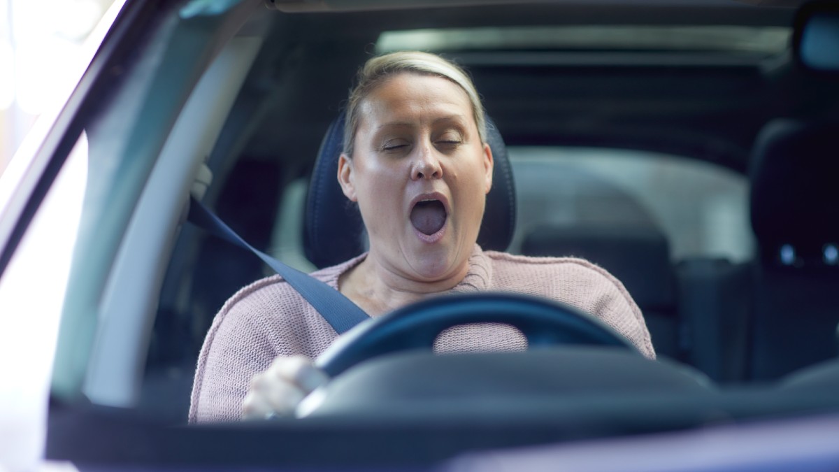 A woman yawning while driving a car