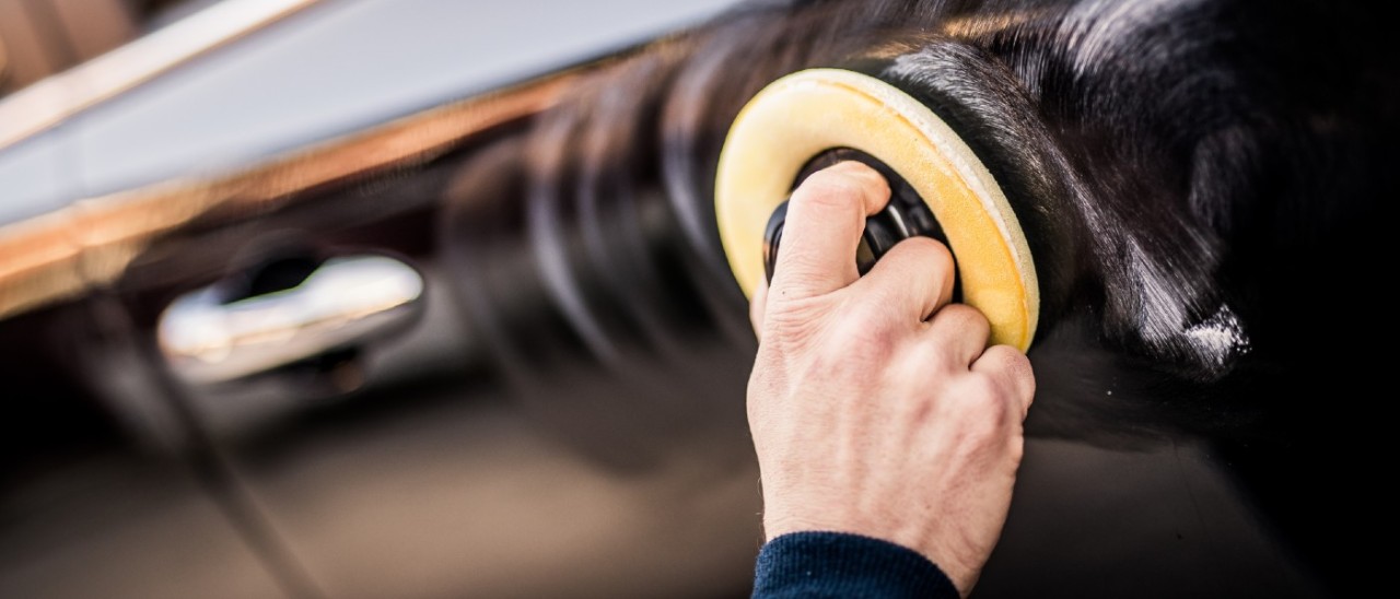 man using a handheld polishing machine on car paint