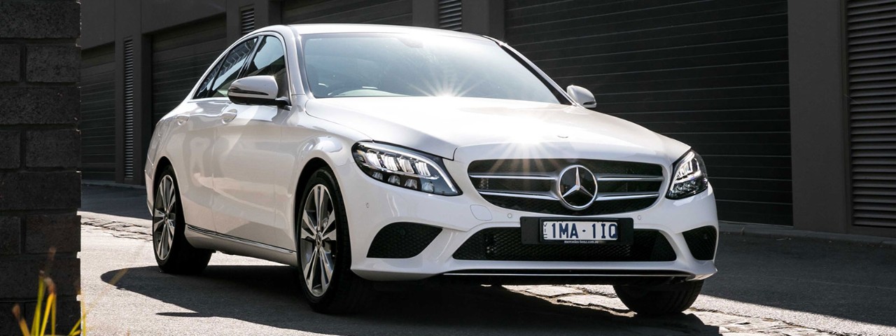 Front side view of a white Mercedes-Benz C 200 car parked in a driveway
