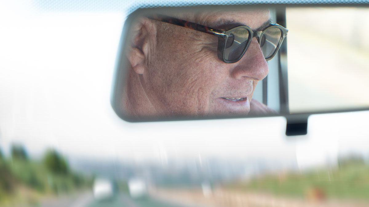 Senior man's face shown in rear vision mirror in car