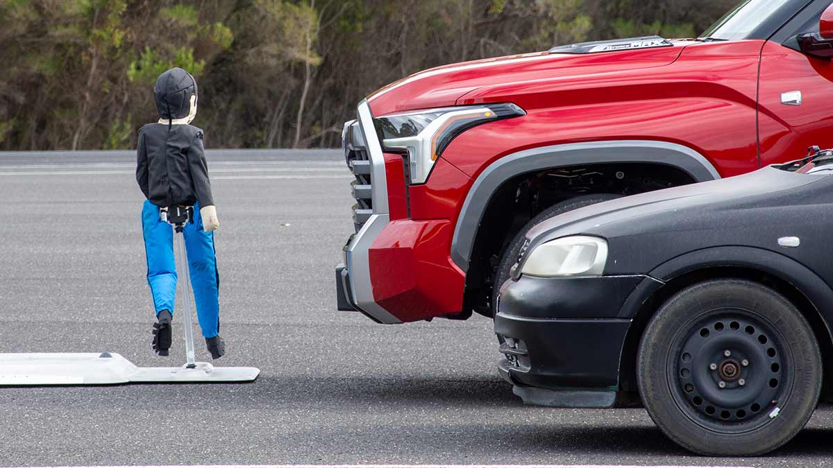 Close-up of red Toyota Tundra pick-up’s front end at head height of child pedestrian dummy crossing in front during ANCAP safety test.