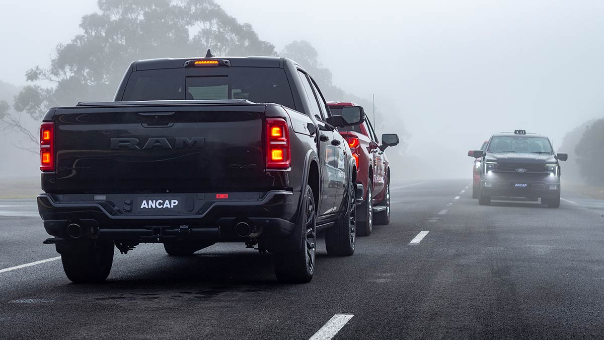 Rear view of black Ram 1500 pick-up at intersection behind red pick-up and with oncoming traffic on foggy road.