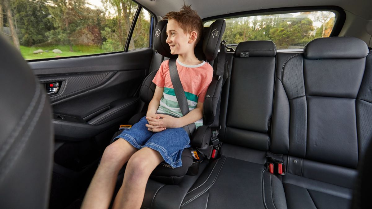 A school-age boy sitting happily in a booster seat and looking out the window
