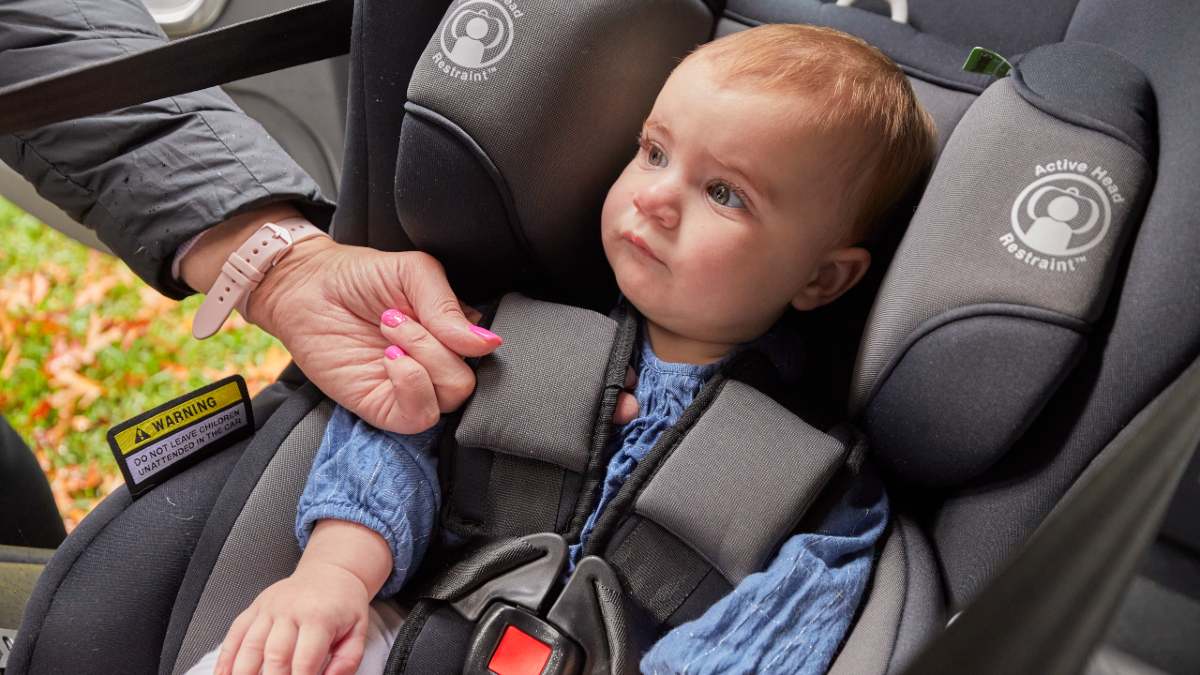 A baby sitting in a car seat while a person checks the tightness of the straps