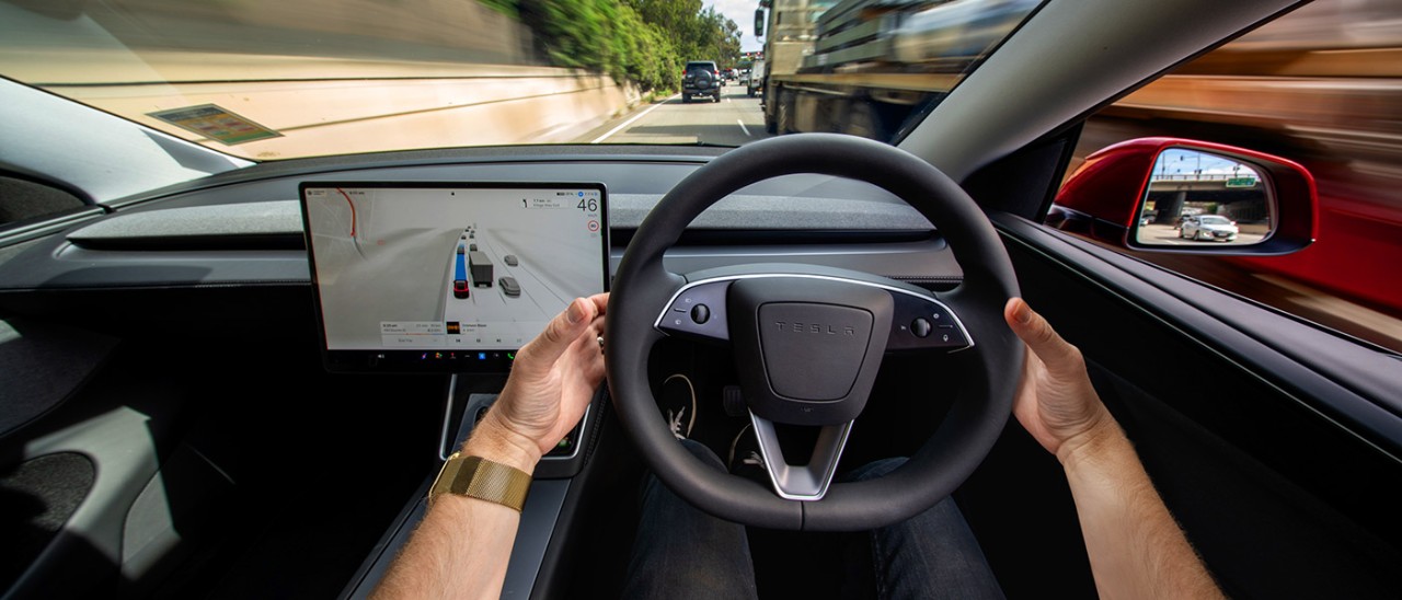 Two hands on steering wheel of Tesla Model Y EV while in Full Self Driving (Supervised) mode on busy Victorian multi-lane freeway.