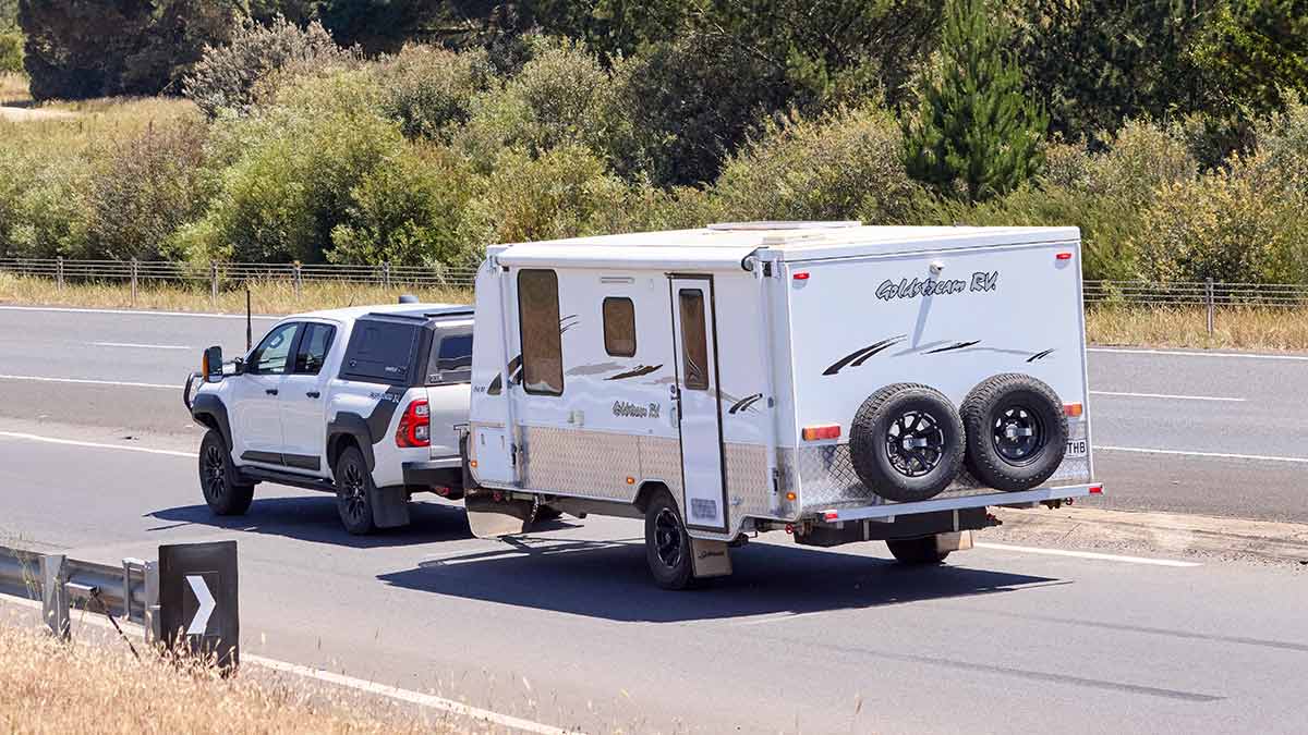 White dual-cab ute with canopy towing white caravan on Western Highway in Victoria