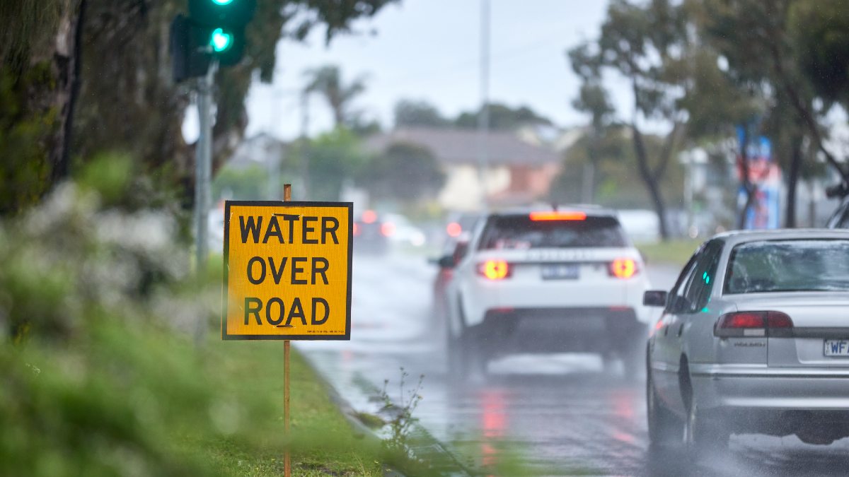 cars driving on wet road; yellow road sign says Water Over Road