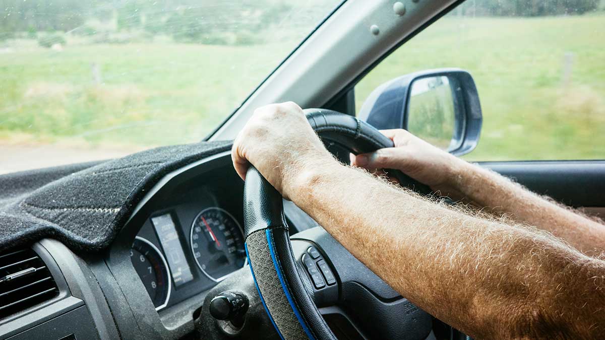 Close-up of man's hands on steering wheel on country road in Australia.