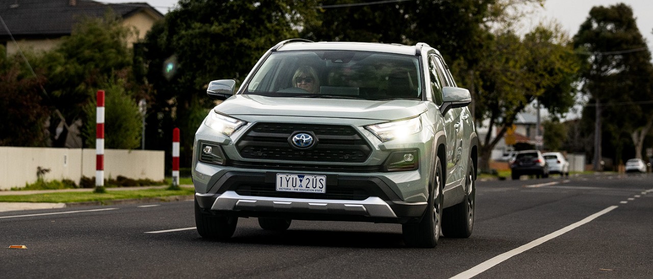 2024-Toyota-RAV4-Edge-Hybrid-RACV-front-action-banner-1400x600 Woman driving light green Toyota RAV4 Edge Hybrid medium SUV on suburban road past children's crossing