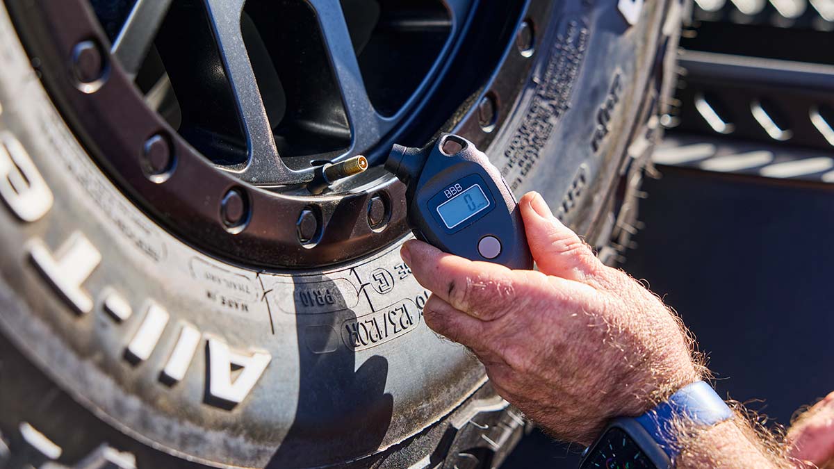 Man checking tyre pressure level on spare tyre at back of off-road caravan using digital tyre pressure gauge