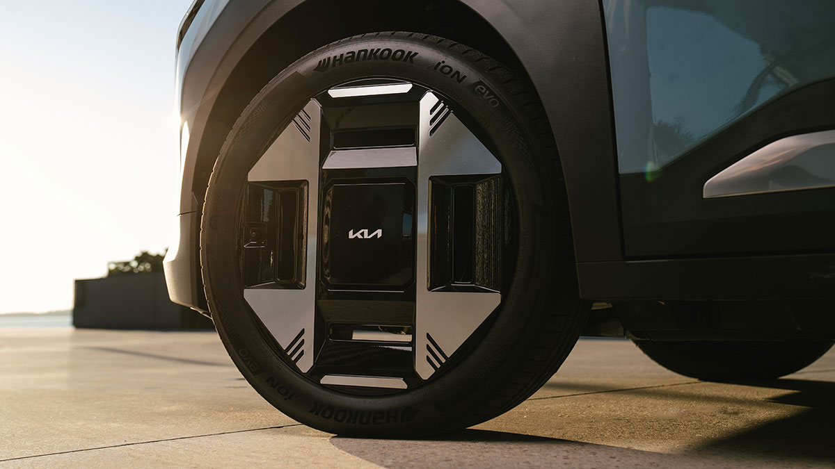 Front left wheel and tyre of Kia EV3 electric car parked on tiled surface with water in distance