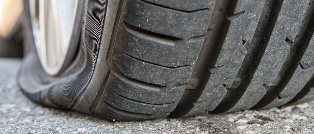 Close-up of flat tyre on back wheel of car on paved surface