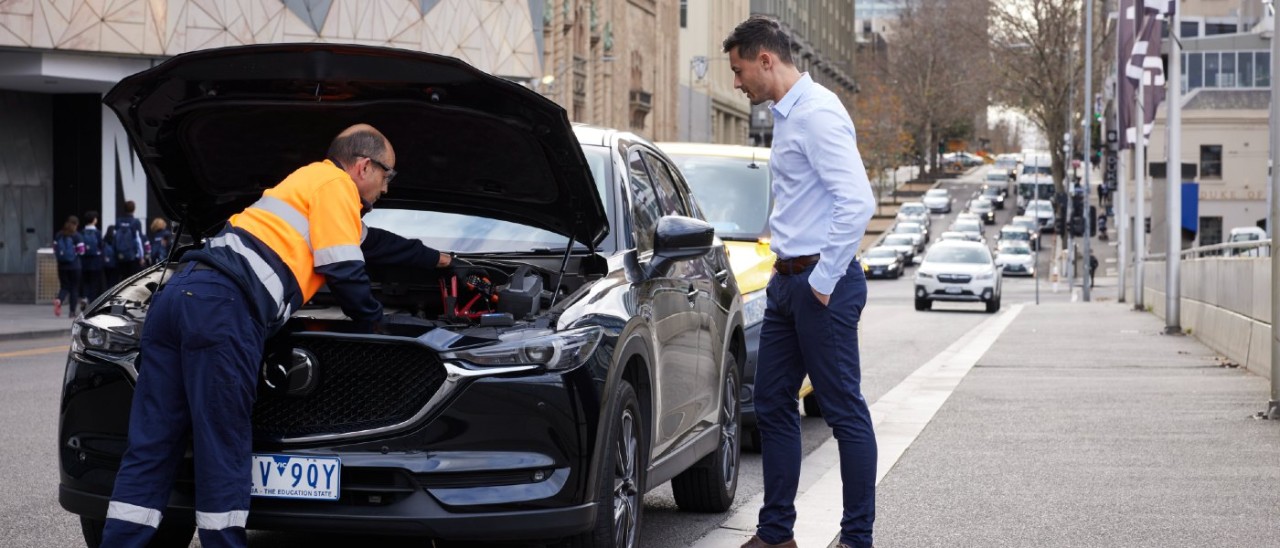 An RACV Emergency Roadside Assistance technician looking under the bonnet of a black SUV parked in the Melbourne CBD