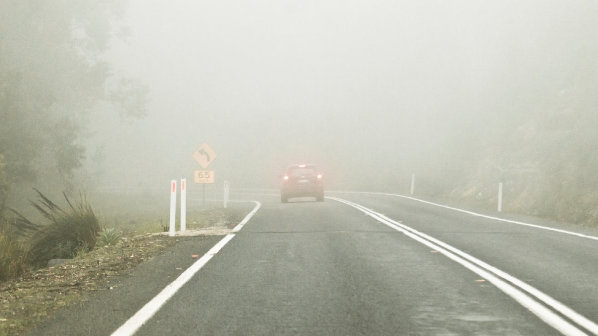 A car driving through thick fog. It is barely visible except for its brake and taillights