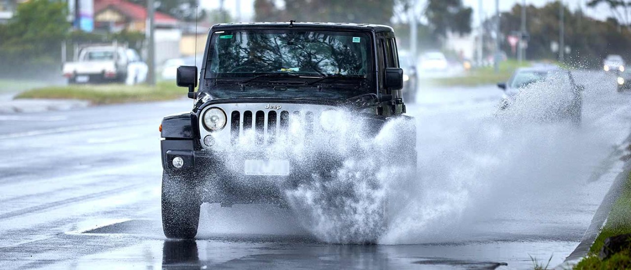 Jeep driving on wet road with water spraying from tyres.