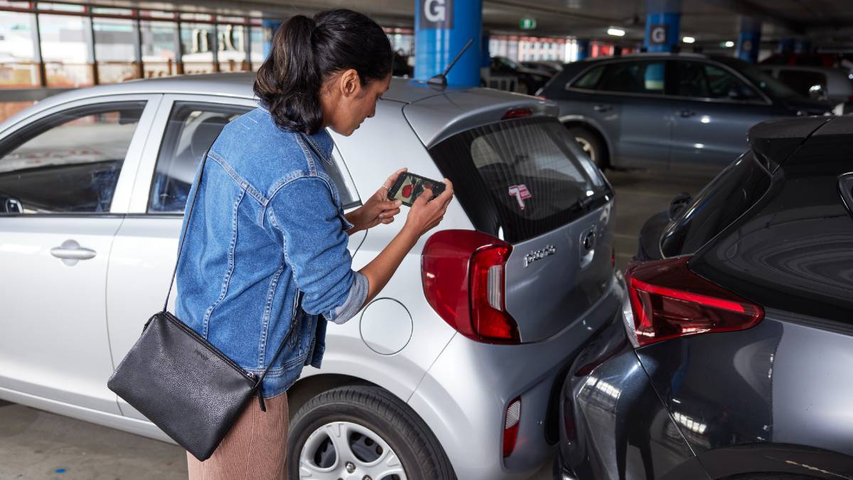 woman taking photo evidence of damage from minor car collision in carpark
