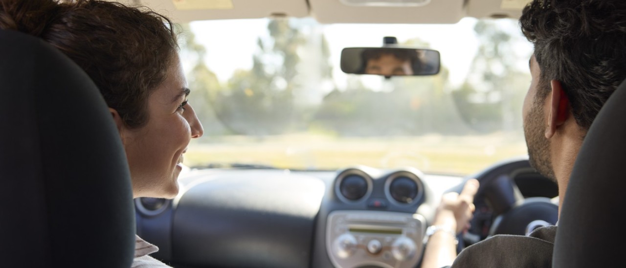 man driving car while woman in passenger seat smiles