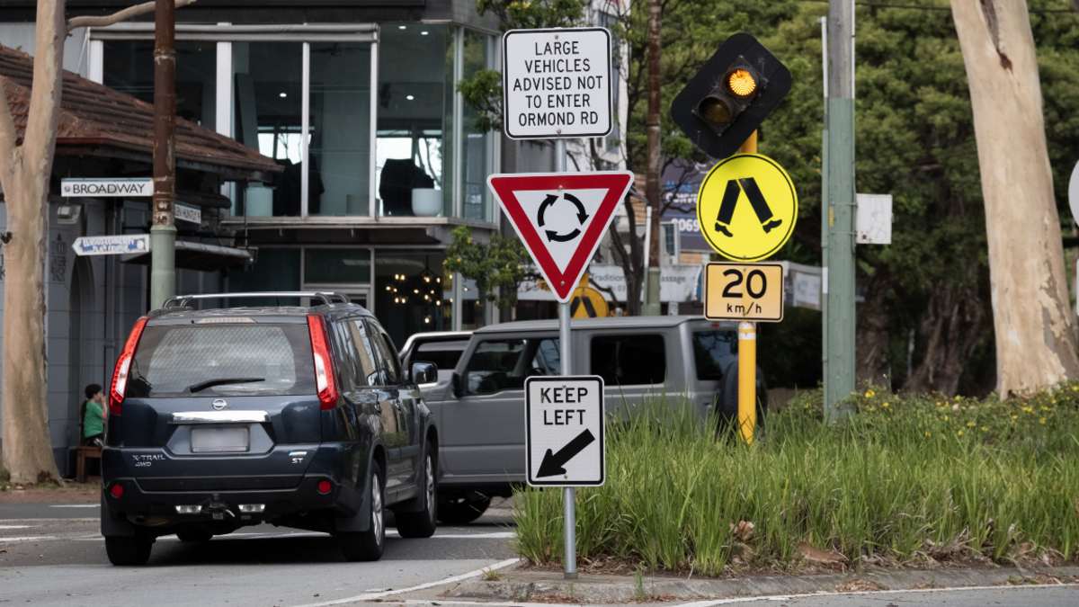 Cars at a roundabout intersection in Elwood with pedestrian crossing signs and yellow lights present
