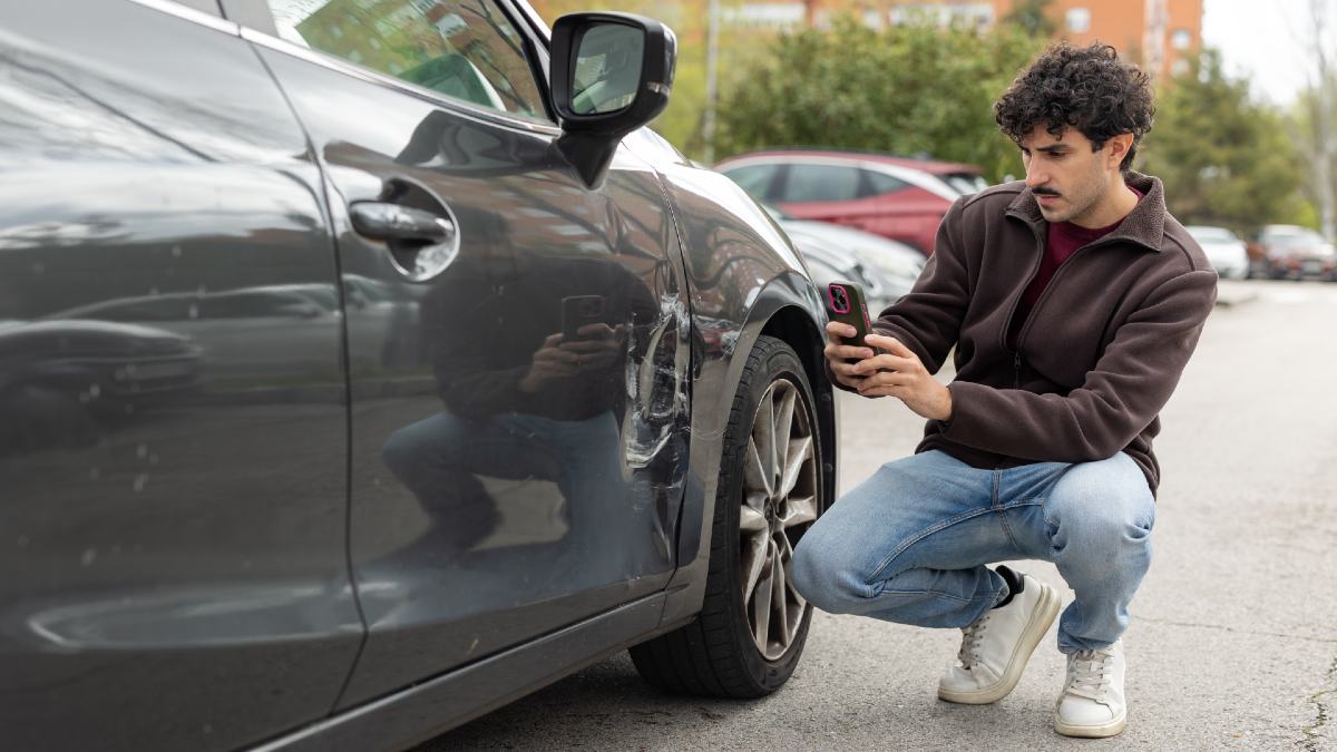 young man taking photo of damage to car after collision