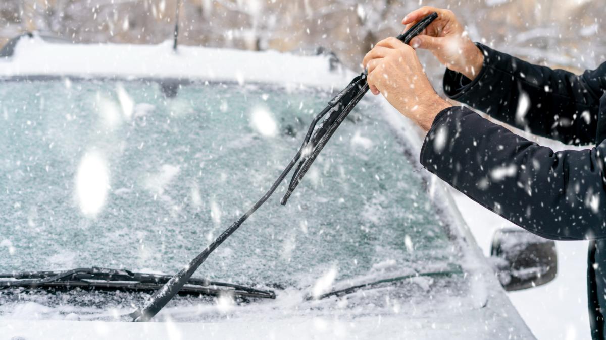 person adjusting windscreen wipers in snow