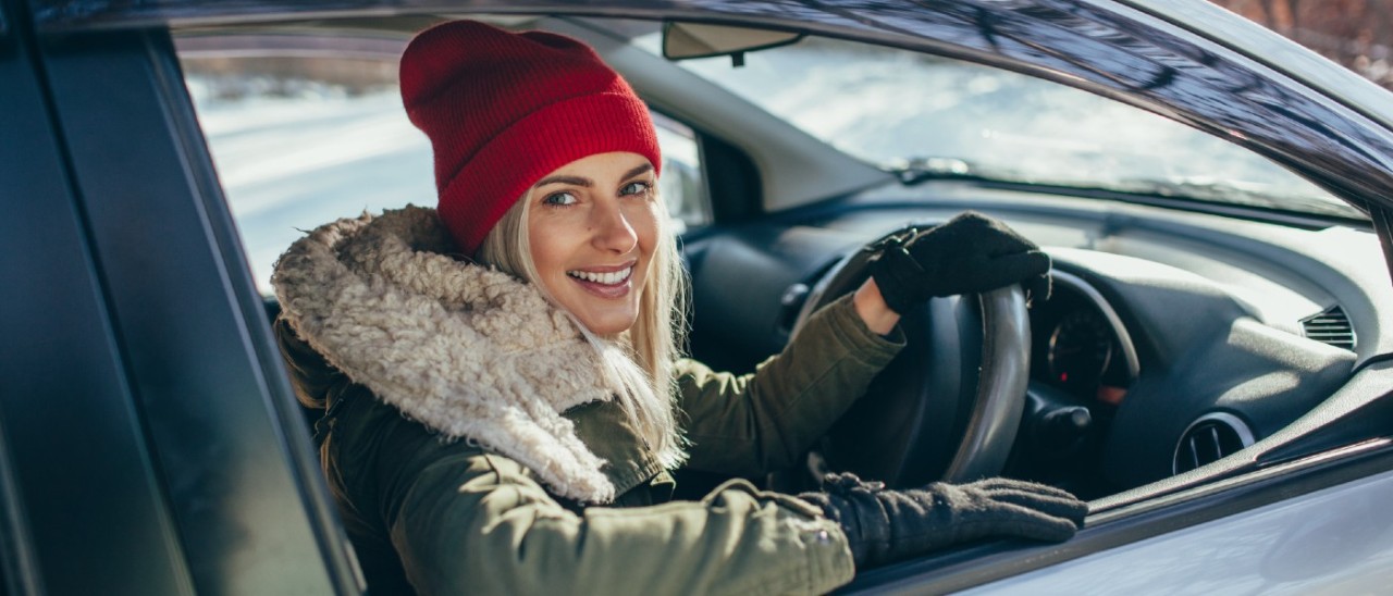 young woman in red beanie and thick winter coat smiling from her parked car