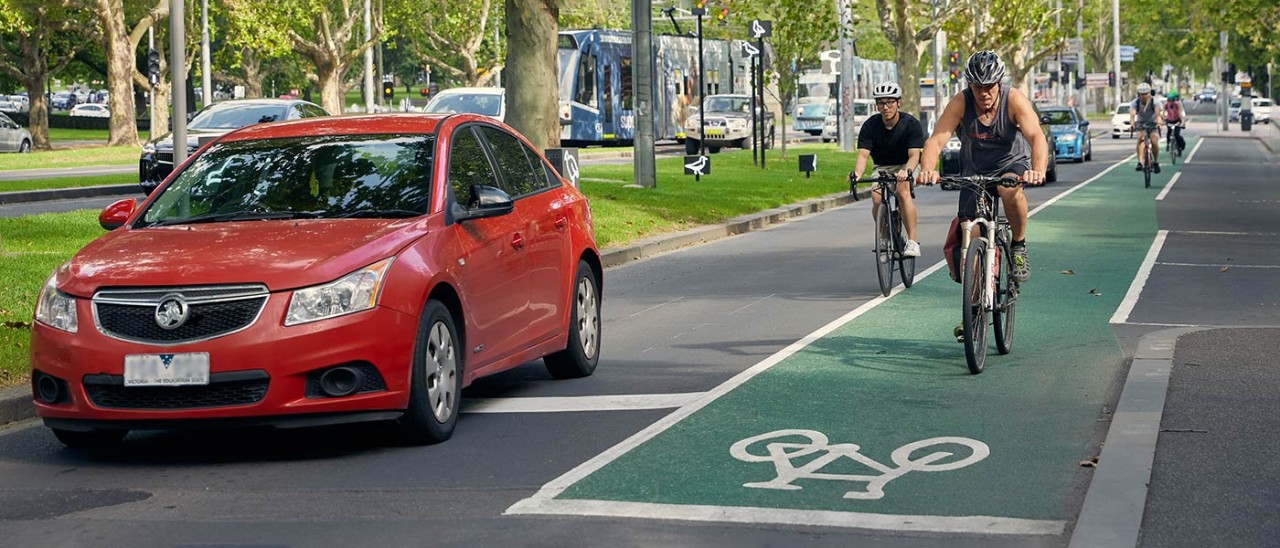 Red car driving alongside cyclists who are on a dedicated bike path on a Melbourne road.