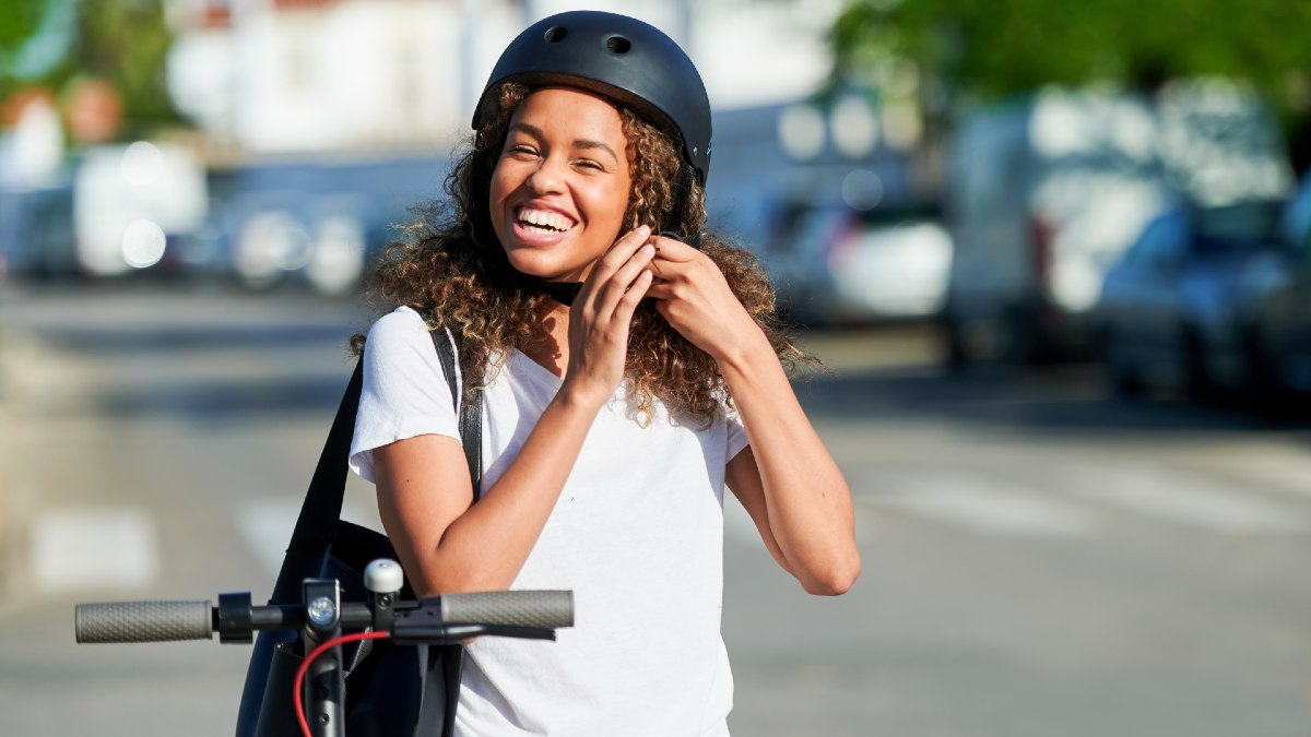 young woman smiling as she puts on a helmet for her e-scooter