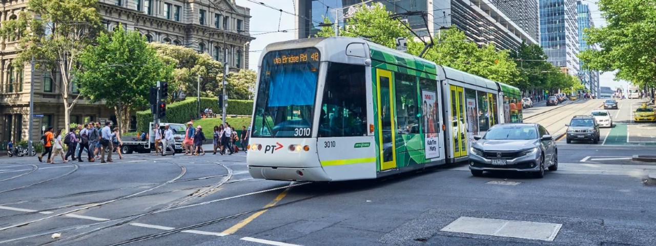 A tram travelling up Collins Street next to car traffic