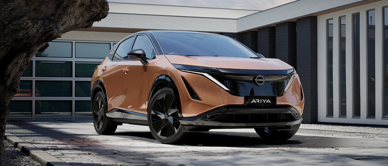 2025-Nissan-Ariya-front-banner-1400x600 Copper-coloured Nissan Ariya medium electric SUV in front of modern house