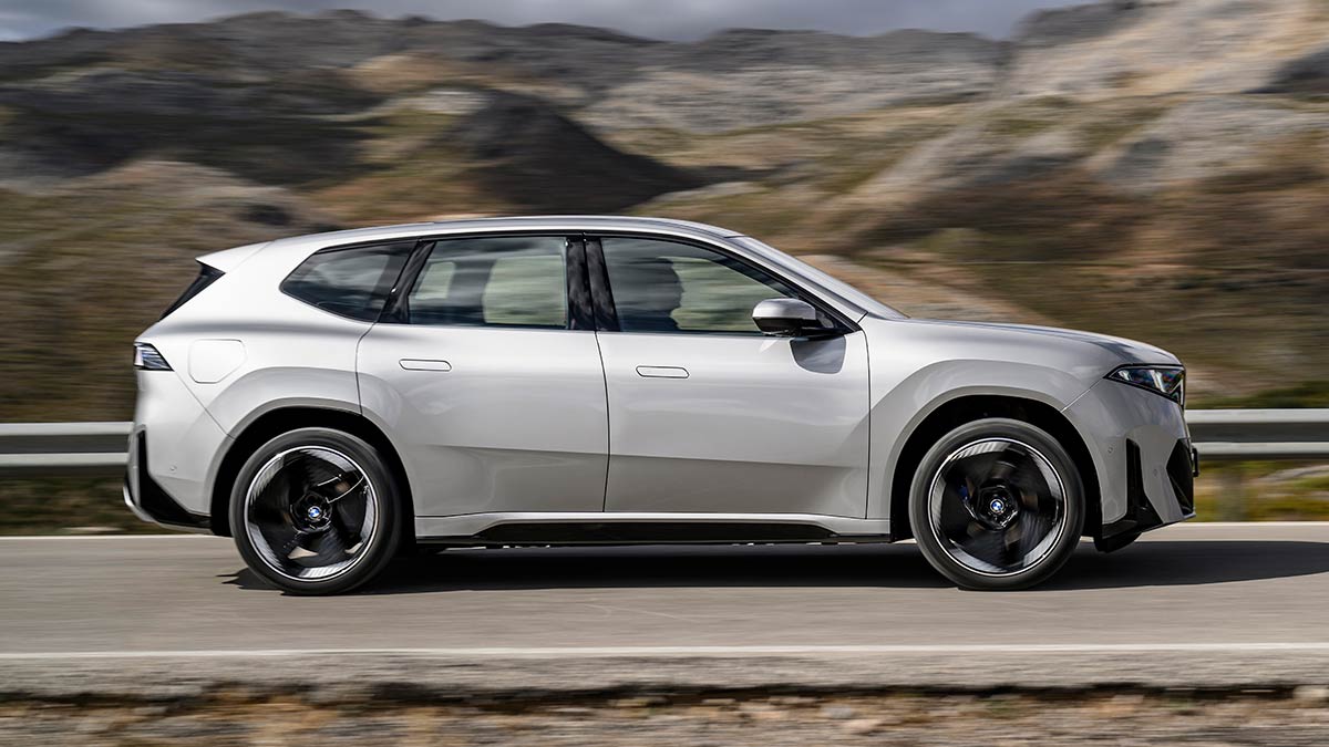 Side-on action shot of silver BMW iX3 50 xDrive SUV on European mountain road.