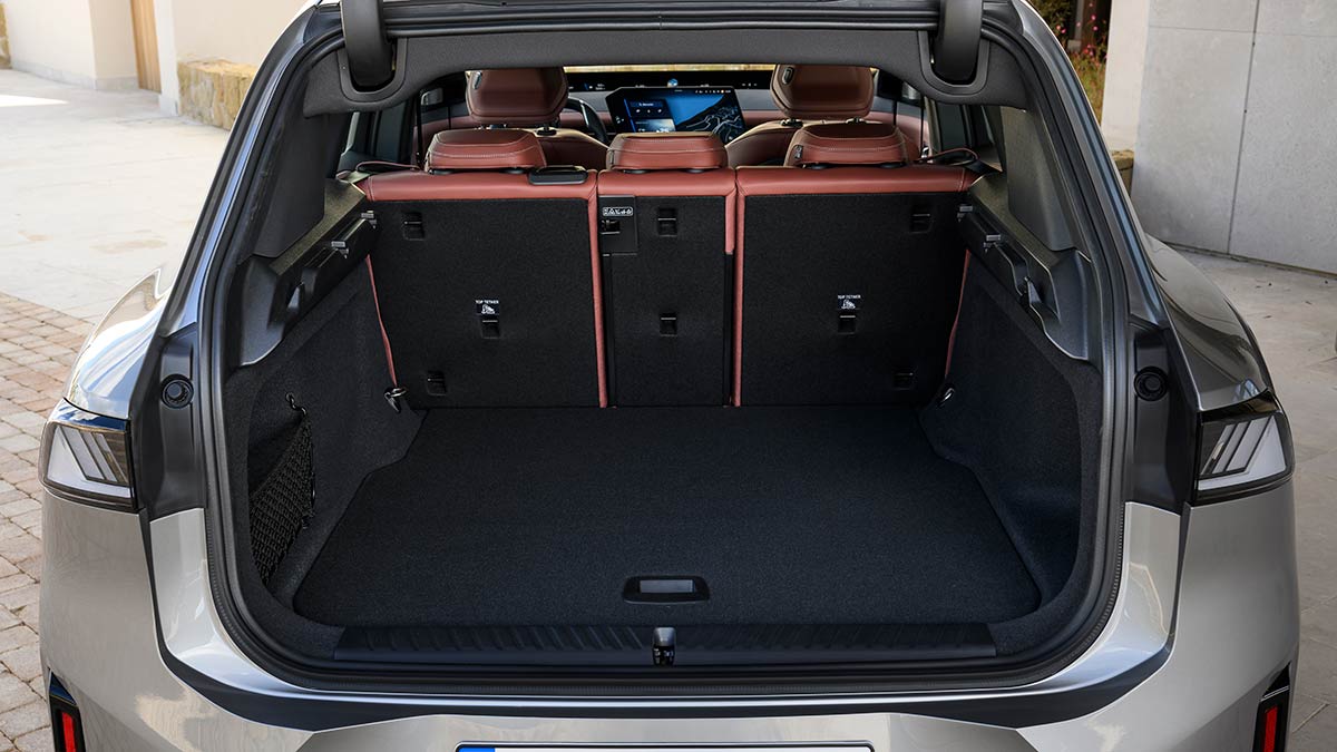 Silver BMW iX3 electric SUV with tailgate open, showing view into cargo area and cabin with 40/20/40 rear seat fold.