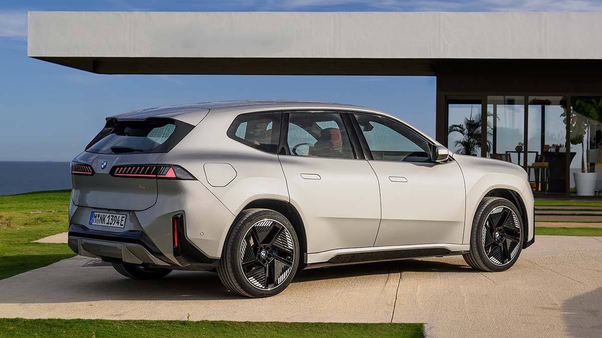 Silver BMW iX3 electric SUV parked in front of modern beachfront house in Europe.