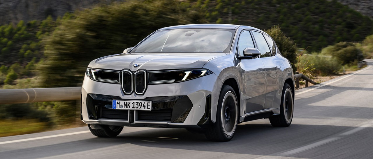 Silver BMW iX3 50 xDrive electric SUV driving through mountainous terrain in Europe.