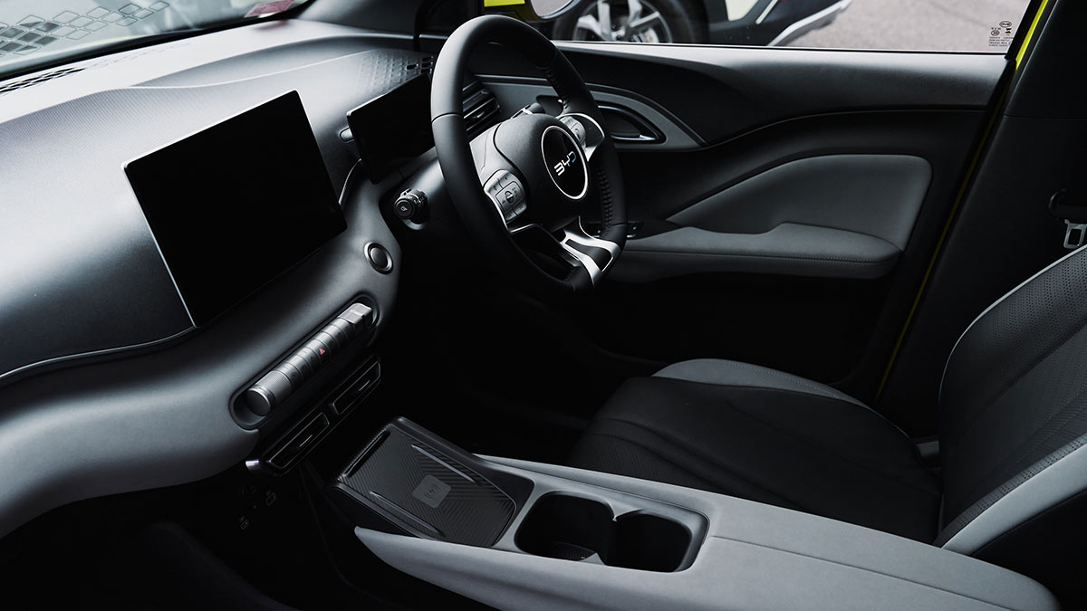 Cabin of BYD Atto 1 with central touchscreen, lower bank of controls, narrow console with charging pad.