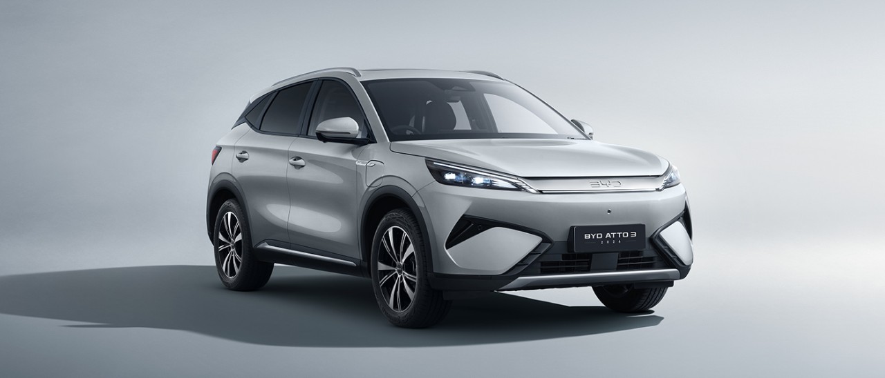 Frontal studio image of white BYD Atto 3 electric SUV with redesigned fascia including LED light strip across car.