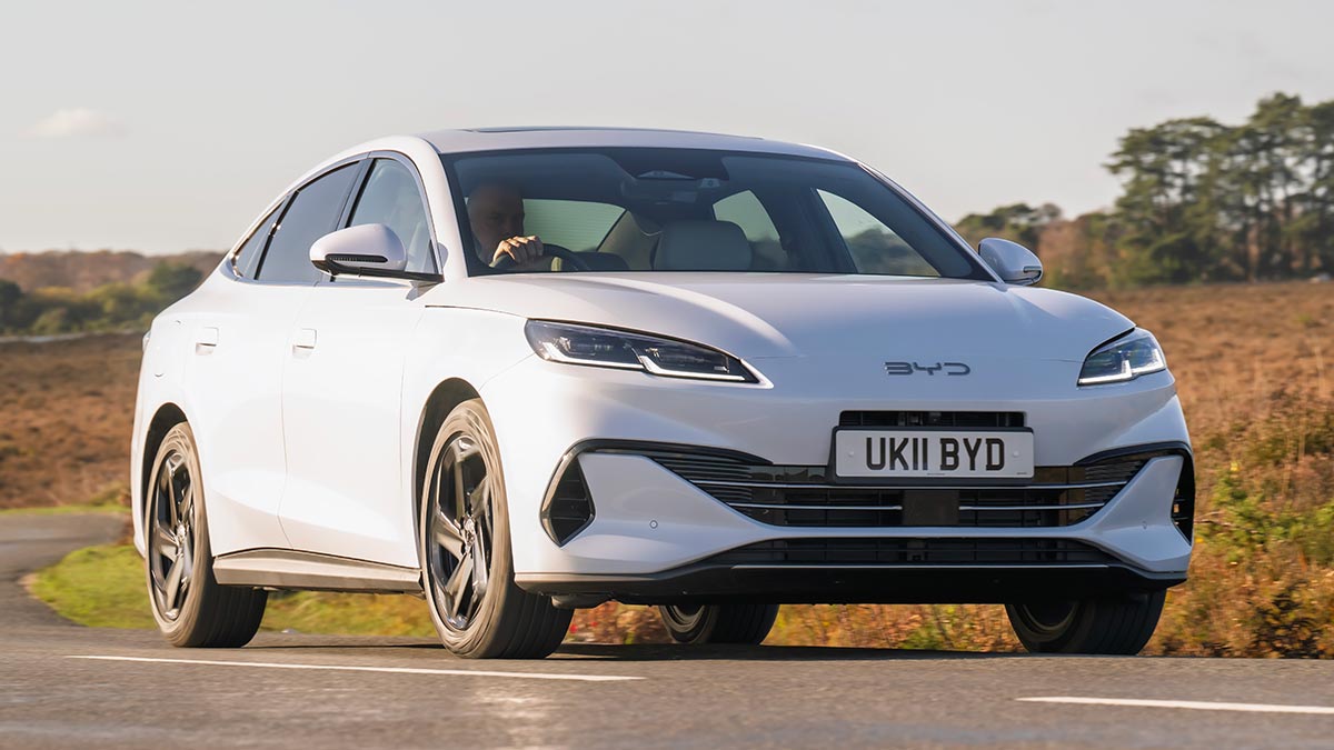 White BYD Seal 6 plug-in hybrid sedan driving through English countryside.
